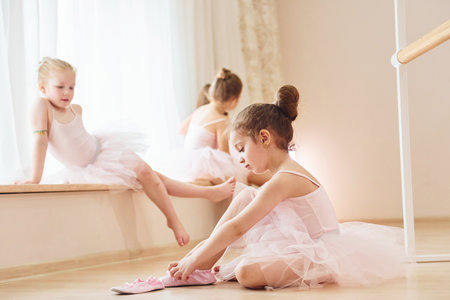Girl sits on the floor. Little ballerinas preparing for performance by practicing dance movesの写真素材