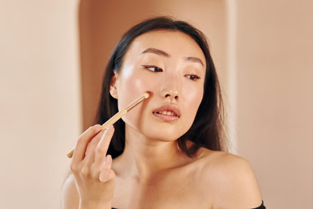 Make up brush. Young serious asian woman standing indoorsの写真素材