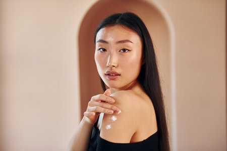 Uses beauty cream. Young serious asian woman standing indoorsの写真素材