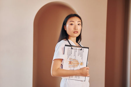 Documents in hands. Young serious asian woman standing indoorsの写真素材