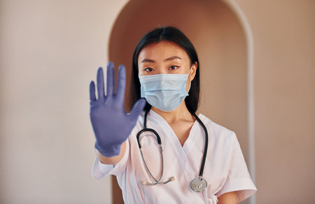 Stop gesture by hand. Young serious asian woman standing indoorsの写真素材