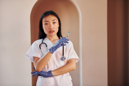 Doctor with syringe. Young serious asian woman standing indoorsの写真素材