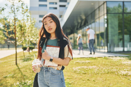 Standing against modern building. Young asian woman is outdoors at daytimeの写真素材