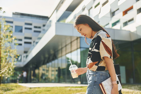 Student walks near modern building. Young asian woman is outdoors at daytimeの写真素材