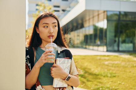 Leaning on the wall. Young asian woman is outdoors at daytimeの写真素材