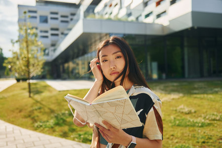With book in hands. Young asian woman is outdoors at daytimeの写真素材