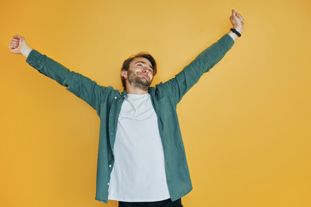 Against yellow background. Young man in casual clothes standing indoors in the studioの写真素材