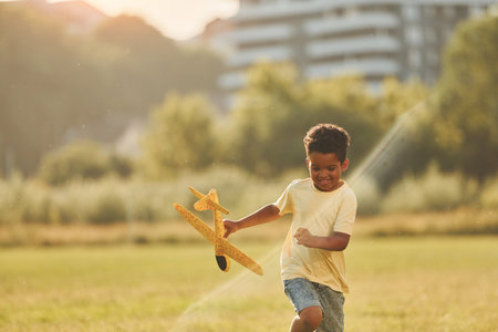Playing with plane. African american kid have fun in the field at summer daytimeの写真素材
