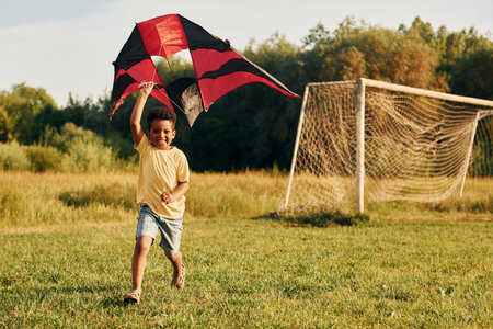 Playing with kite. African american kid have fun in the field at summer daytimeの写真素材