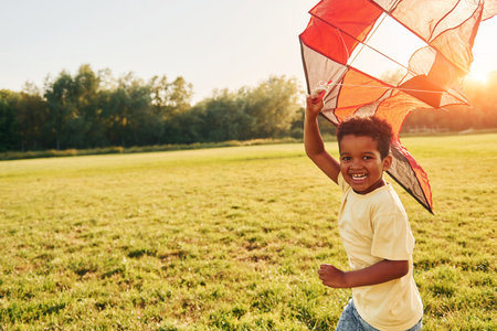 Playing with kite. African american kid have fun in the field at summer daytimeの写真素材