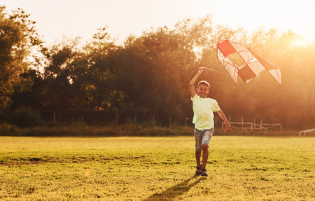 Playing with kite. African american kid have fun in the field at summer daytimeの写真素材
