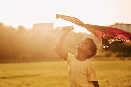 Red kite. African american kid have fun in the field at summer daytimeの写真素材