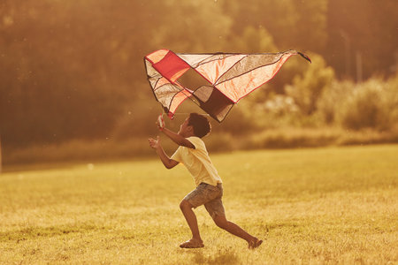Running with red kite. African american kid have fun in the field at summer daytimeの写真素材