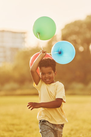 With balloons in hands. African american kid have fun in the field at summer daytimeの写真素材