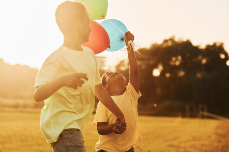 Playing with air balloons. Two african american kids have fun in the field at summer daytime togetherの写真素材