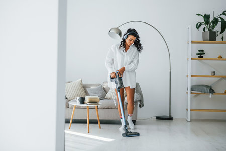 Uses vacuum cleaner. Woman in casual clothes is indoors at homeの写真素材