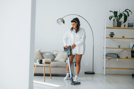 Uses vacuum cleaner. Woman in casual clothes is indoors at homeの写真素材