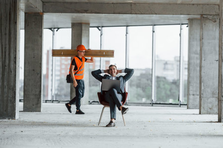 Moving object. Man in suit and handyman in orange protective wear is working on constructionの写真素材