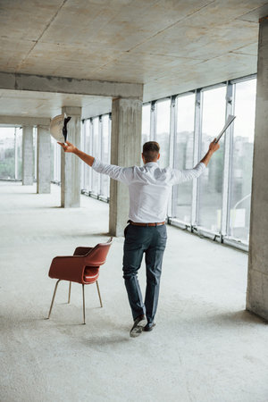 Near the chair. Young man in formal wear is working indoors on the construction