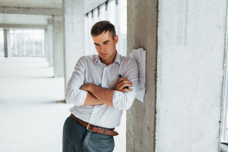 Documents on the pillar. Young man in formal wear is working indoors on the constructionの写真素材