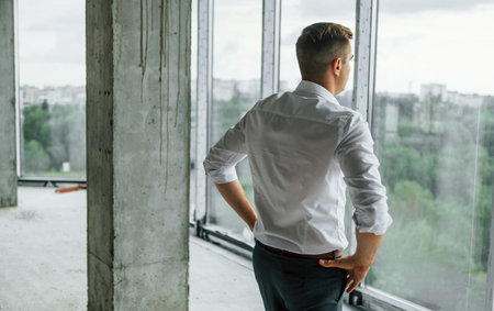 Big window. Young man in formal wear is working indoors on the construction