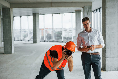 Planning the process. Man in suit and handyman in orange protective wear is working on constructionの写真素材