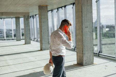 Walks and talks. Young man in formal wear is working indoors on the constructionの写真素材