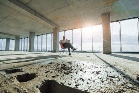 Beautiful sunlight goes through big window. Young man in formal wear is working indoors on the constructionの写真素材