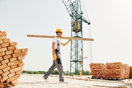With wooden plank. Young construction worker in uniform is busy at the unfinished buildingの写真素材
