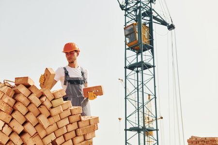 With wooden plank. Young construction worker in uniform is busy at the unfinished building