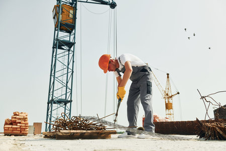 Crane is at background. Young construction worker in uniform is busy at the unfinished building