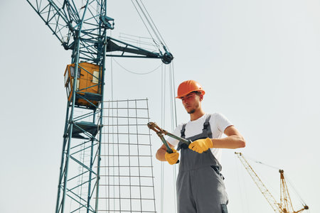 Crane is at background. Young construction worker in uniform is busy at the unfinished buildingの写真素材