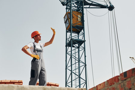 Communicationg with someone. Young construction worker in uniform is busy at the unfinished buildingの写真素材