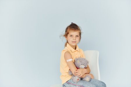 Little girl sitting on the chair against white background after vaccinationの写真素材