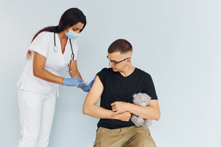 Man holding teddy bear during procedure. Doctor in uniform making vaccination to the patientの写真素材