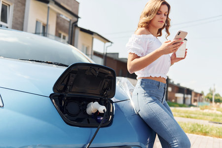 Waiting for the charge to finish. Young woman in casual clothes with her electromobile outdoors at daytimeの写真素材