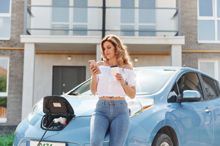 Waiting for the charge to finish. Young woman in casual clothes with her electromobile outdoors at daytimeの写真素材