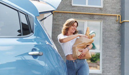 Holding products in bag. Young woman in casual clothes with her electromobile outdoors at daytimeの写真素材