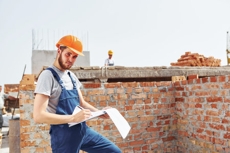 Busy day. Young construction worker in uniform is busy at the unfinished building