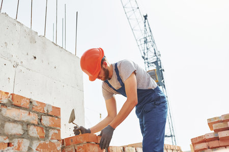 Young construction worker in uniform is busy at the unfinished building