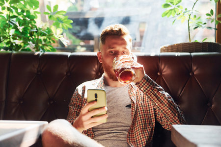 Smartphone in hand. Man in casual clothes sitting in the pubの写真素材