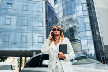Holding black notepad. Woman in formal wear standing outdoors in the city at daytimeの写真素材