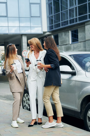 Women in formal wear is outdoors in the city together standing near silver colored carの写真素材