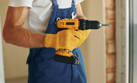 Using tool. Young man working in uniform at construction at daytimeの写真素材