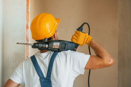 Using tool. Young man working in uniform at construction at daytimeの写真素材