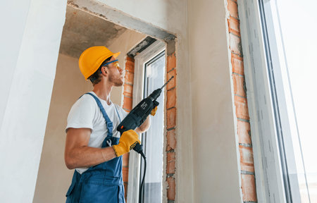 In hard hat. Young man working in uniform at construction at daytime