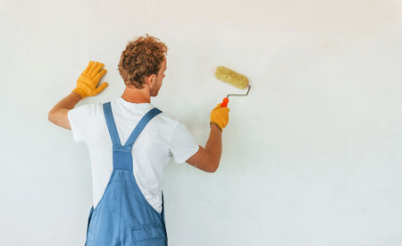 Clean walls. Young man working in uniform at construction at daytimeの写真素材