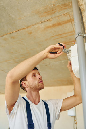 Repaiting the pipes. Young man working in uniform at construction at daytimeの写真素材