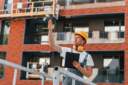 Holding notepad with plan. Young man working in uniform at construction at daytimeの写真素材