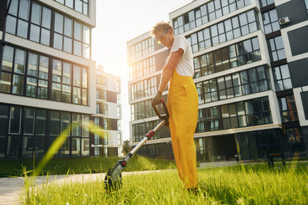 Beautiful sunshine. Man cut the grass with lawn mover outdoors in the yardの写真素材